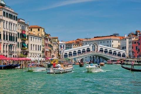 VENICE, ITALY, JULY 19, 2019: Rialto bridge with boats and gondolas passing under on Grand Canal,