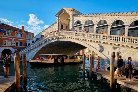 VENICE, ITALY, JUNE 27, 2018: Rialto bridge with vaporetto passing under on Grand Canal on sunset,