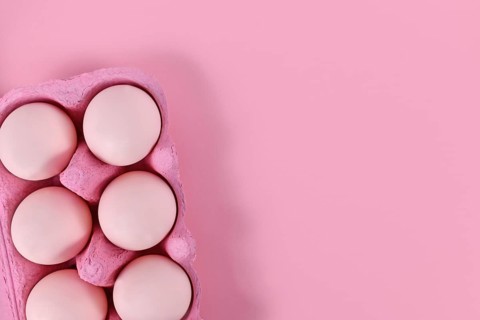 Easter eggs in box on pink background with copy space
