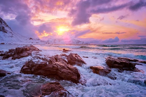 Waves of Norwegian sea on rocky coast in fjord on sunset with sun. Skagsanden beach, Lofoten
