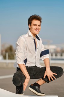 Young man in unfastened white shirt sits on squats on the street