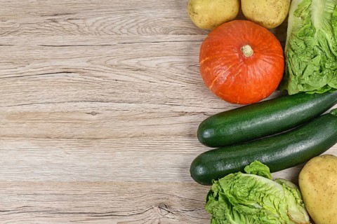 Healthy raw Hokkaido squash, zucchini, lettuce and potatoes on side of wooden background with empty