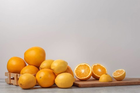 Basket and wooden board with oranges and lemons, vitamin C, light background, copy room