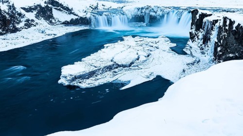 Ice layer in the river Skialfandaljot, behind it the waterfall Godafoss, Northern Iceland Eyestra,