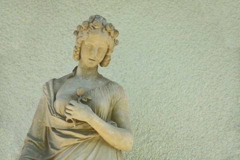 Sculpture of a woman with hair ornament and rose, flower in arm, holding hand, stone, yellow,