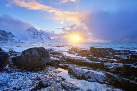 Beach of Norwegian sea on rocky coast in fjord on sunset in winter. Vareid beach, Lofoten islands,