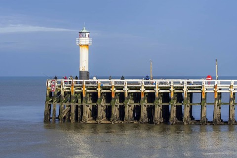 Sea anglers with large fishing rods casting their lines from wooden pier, jetty at the Nieuwpoort,