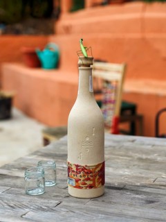 Bottle of mezcal with praying mantis (Mantis religiosa) and two glasses on a simple wooden table,