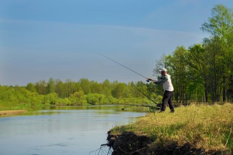 Man fish with spinning on river bank, casting lure. Outdoor weekend activity. Photo with shallow