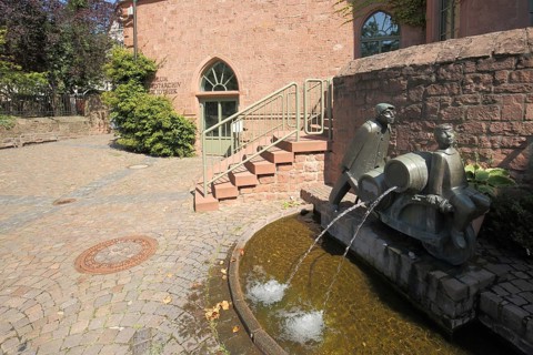 Ornamental fountain with two figures, wheelbarrows loaded with barrels and local history museum in
