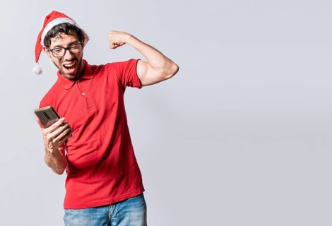 Smiling young man in christmas hat using cellphone celebrating. Happy guy in christmas hat looking