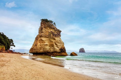 Sandy beach beach with a large rock formation in the sea, under a slightly cloudy sky, Cathedral