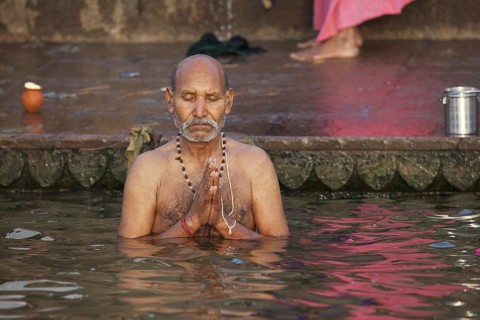 Indian man bathing and praying in the Ganges river at a ghat at Varanasi, Uttar Pradesh, India,