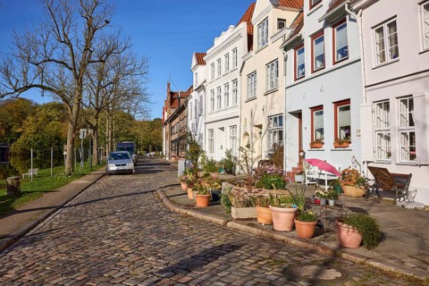 Street An der Obertrave with historic buildings, cobblestone pavement, bare trees, flower pots with