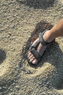 Close-up of man's foot in sandal standing on beach with coarse sea sand grains