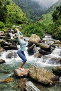 Young sporty fit woman doing yoga asana Utkatasana (chair pose) outdoors at tropical waterfall
