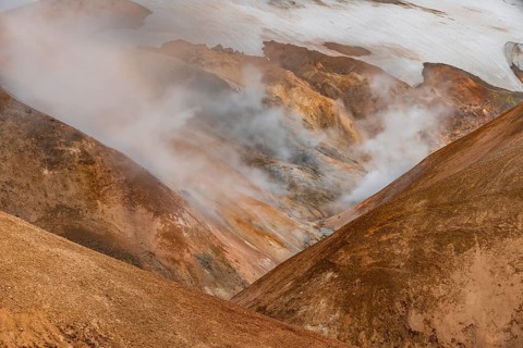 Steaming stream between colourful rhyolite mountains and snowfields, Hveradalir geothermal area,