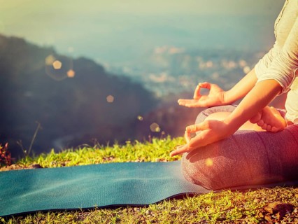 Close up of woman in Padmasana yoga lotus pose with chin mudra outdoors with copyspace. With light