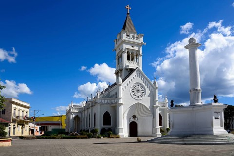 White church with pointed tower on a sunny square under a blue and white sky, Church of San Pedro