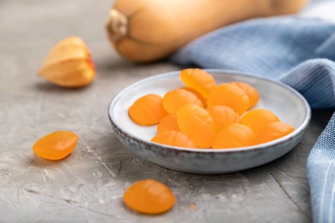Jelly pumpkin candies on gray concrete background and blue linen textile. close up, side view,