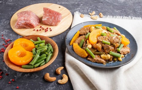 Fried pork with peaches, cashew and green beans on a black concrete background. side view, close