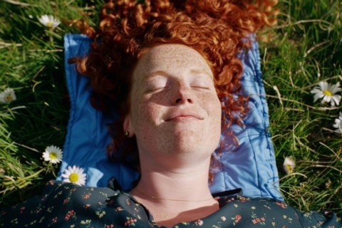 Teenager, young fair-skinned woman with red hair and freckles lying on a spring meadow and basking