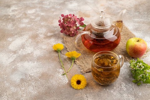 Red tea with herbs in glass teapot on brown concrete background and linen textile. Healthy drink