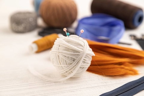 Sewing accessories: scissors, thread, thimbles, braid on white wooden background. Side view, close
