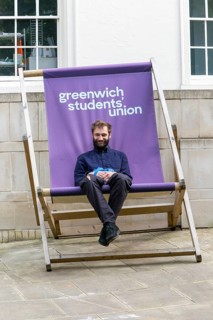 Young man sitting in giant deckchair outside the Students' Union, Greenwich, London SE10, England,