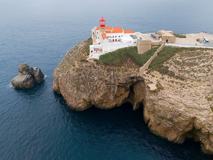 A red lighthouse and white buildings on a rocky cliff overlooking the ocean, an isolated feeling,