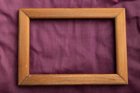 Wooden frame on smooth cotton purple tissue. Top view, flat lay, natural textile background and