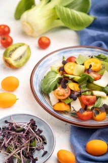 Vegetarian salad of pac choi cabbage, kiwi, tomatoes, kumquat, microgreen sprouts on a white