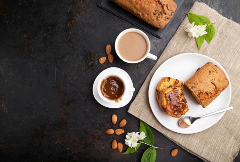 Homemade cake with raisins, almonds, soft caramel and a cup of coffee on a black concrete
