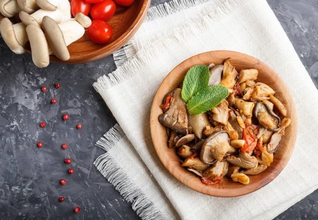 Fried oyster mushrooms with tomatoes in wooden plate on black concrete background. top view, close