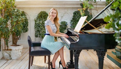A pianist in a light-coloured dress plays music on a grand piano in an elegantly decorated room