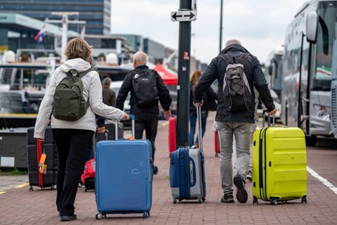 Travellers on their way to a river cruise ship at the quay of the Ij, transporting their luggage,
