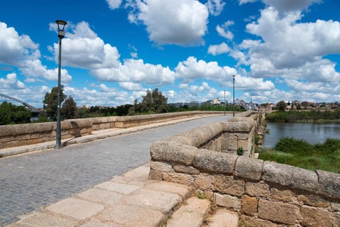 View of an old stone bridge with cobblestones against a clear blue sky and white clouds, Roman
