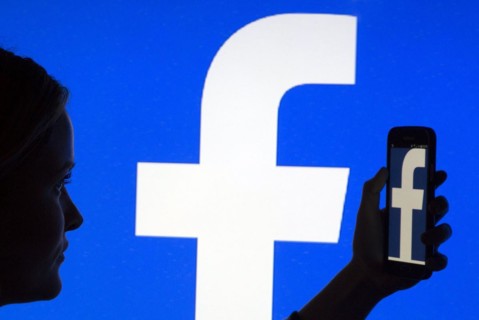 Silhouette of a woman with a smartphone in her hand in front of a Facebook logo, 12/01/2016
