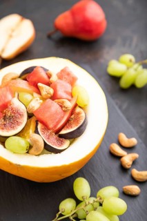 Vegetarian fruit salad of watermelon, grapes, figs, pear, orange, cashew on slate board on a black