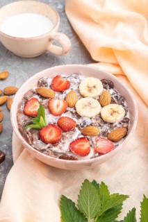Chocolate cornflakes with milk, strawberry and almonds in ceramic bowl on gray concrete background