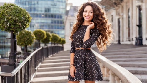 Smiling woman in a polka dot dress stands on a city staircase with modern buildings, AI generated,