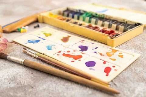 Drawing accessories set: brushes, pencils, watercolor on brown concrete background. Side view,