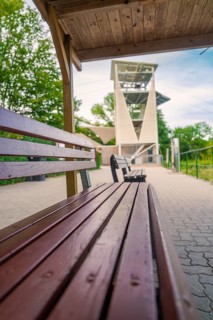 A wooden bench next to a hiking trail offers a view of a large modern observation tower,