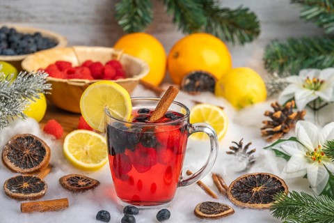 Punch in a glass cup, surrounded by oranges, lemons, raspberries and Christmas decorations