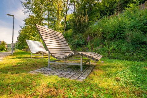 Several wooden loungers in a sunny park surrounded by green vegetation, Nagold, Black Forest,