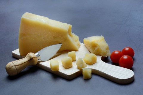 A piece of Parmesan cheese and chopped pieces of cheese on a wooden board