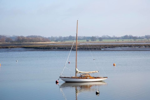 One yacht moored off muddy shore calm water River Deben, Waldringfield, Suffolk, England, UK