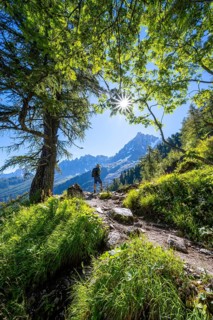 Hiker on hiking trail with sun star, hiking trail La Jonction, behind summit of Aiguille du Midi,
