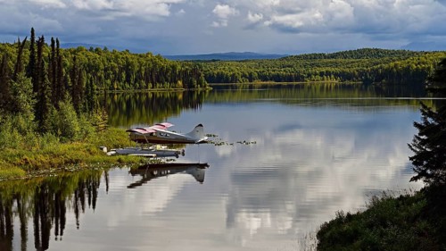 Seaplane Beaver de Havilland stands on the shore of a crystal-clear lake and is reflected in the