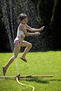 Young girl refreshing herself under a lawn sprinkler, Federal Republic of Germany